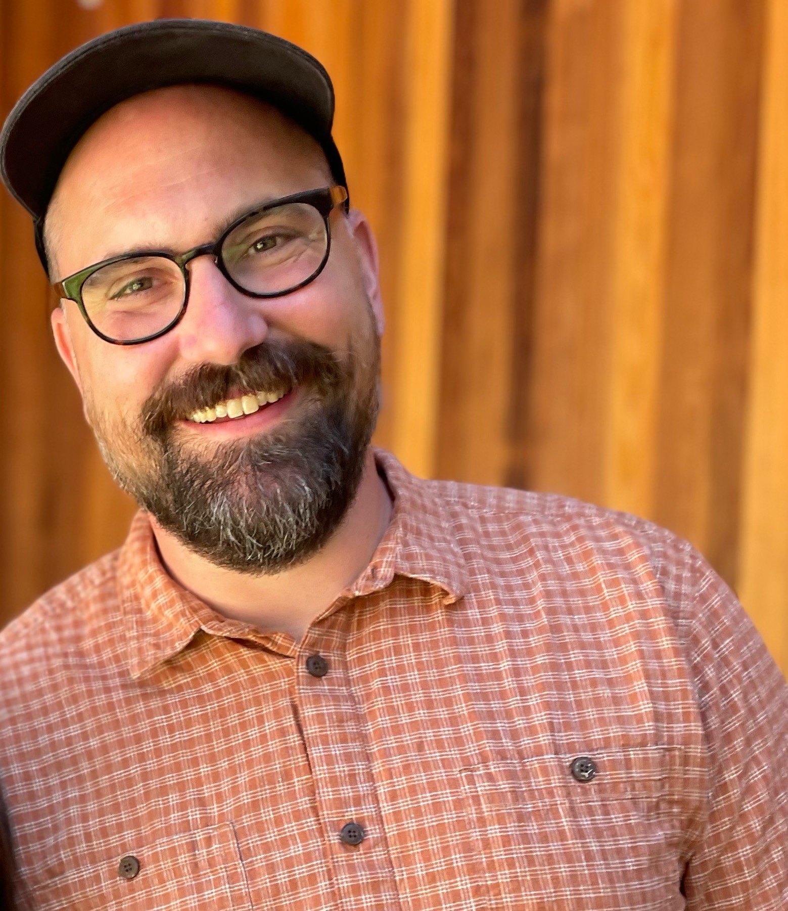 photo of Ben Cushing wearing a black hat, black glasses and a red and white checkered button down shirt