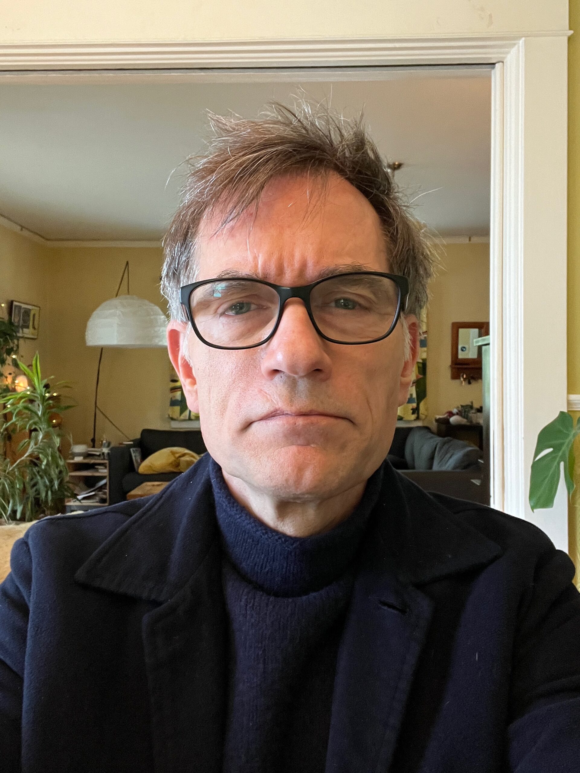 Image of Michael Annus wearing a navy blue turtleneck and navy blue jacket and glasses.